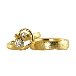 Asymmetrical gold wedding rings with a raw surface and a playful curl enclosing two diamonds