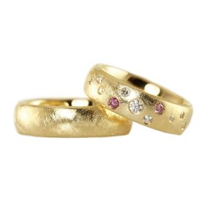 Wide wedding rings in gold with a rough surface and a sprinkling of small diamonds in white and pink