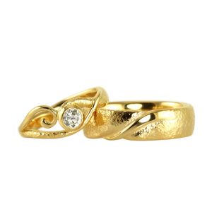 Beautiful handmade wedding rings in gold with a scroll and large white diamond and a rough surface.